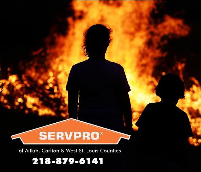 Two children are silhouetted against the backdrop of a structure fire blazing in the distance at night. 